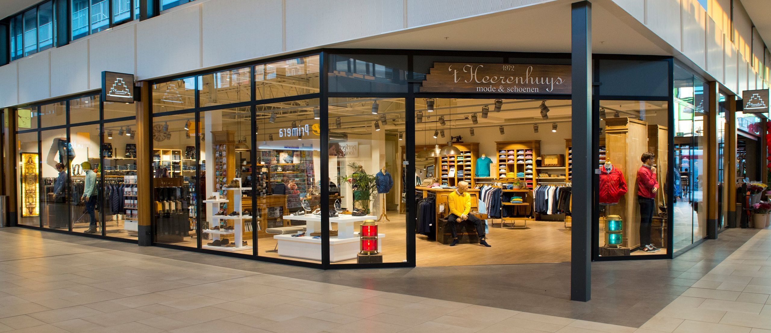 De winkelgevel van ’t Heerenhuys Mode & Schoenen in Winkelcentrum Kerkelanden, met grote etalageramen en zicht op de houten wandkasten binnen.